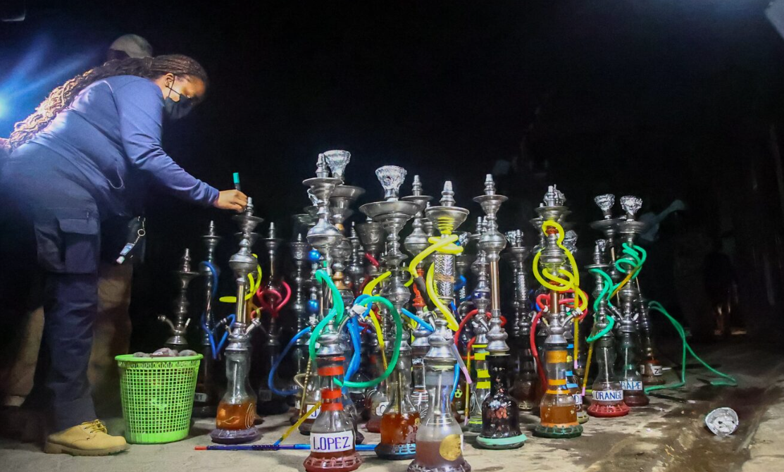 An officer parades the confiscated shisha bongs outside Yejoka Garden Restaurant in Kilimani, Nairobi on December 22, 2023 when the Authority led by the CEO Dr. Anthony Omerikwa, MBS, raided the entertainment joint 